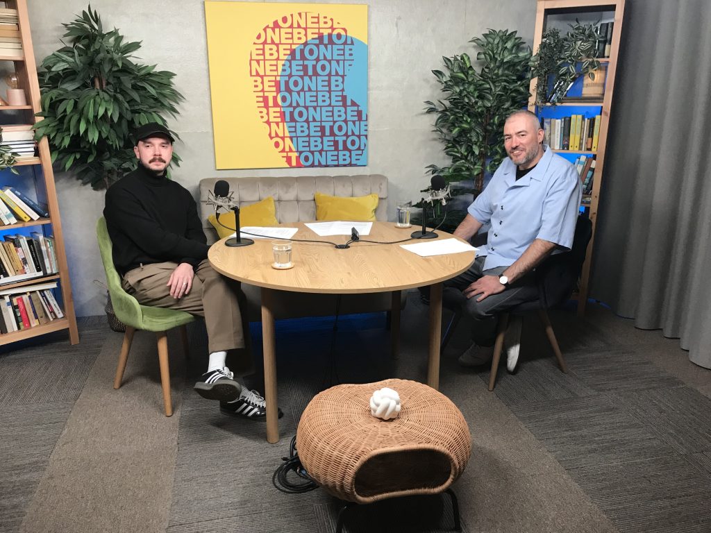Two people are sitting at a round table in a minimalist, artistic studio.