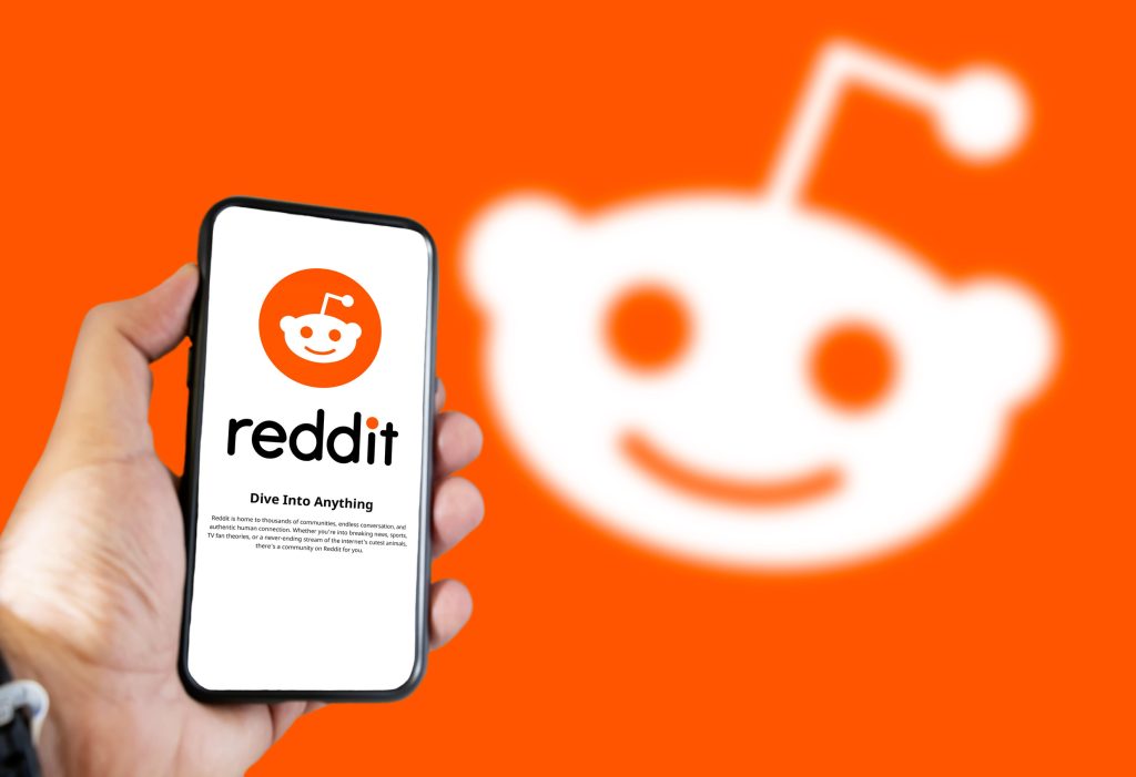 A hand holding a phone with a Reddit logo on its screen.